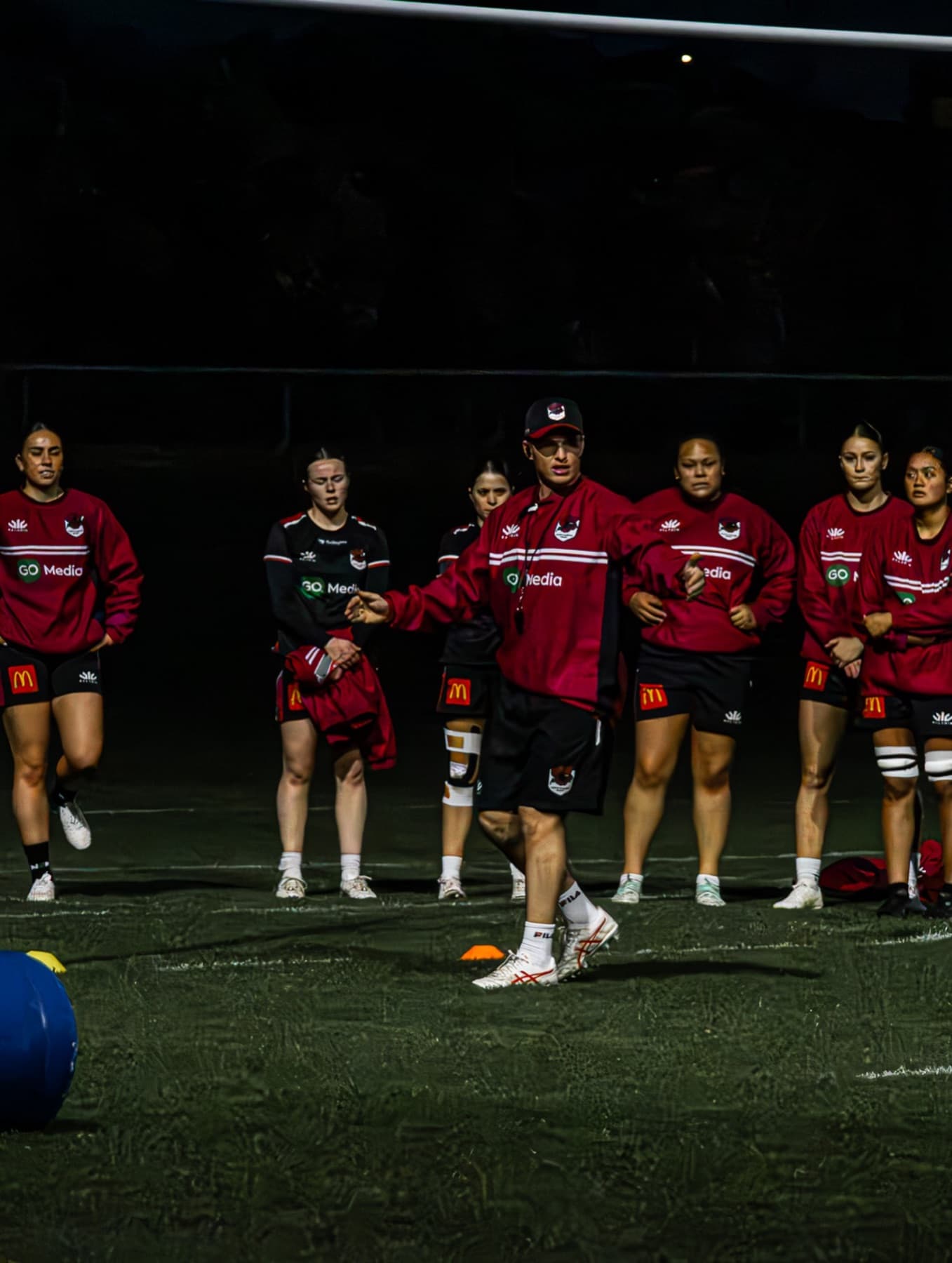 Logan Brown briefing a women's rugby squad at night training.